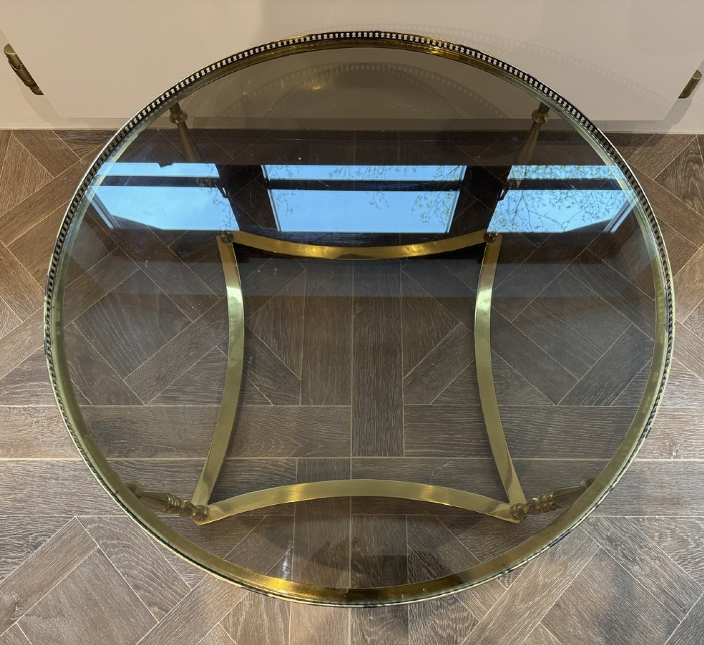 A circular brass coffee table featuring a dark smoked glass top, a pierced gallery rim, turned legs, and a curved stretcher base. View IV