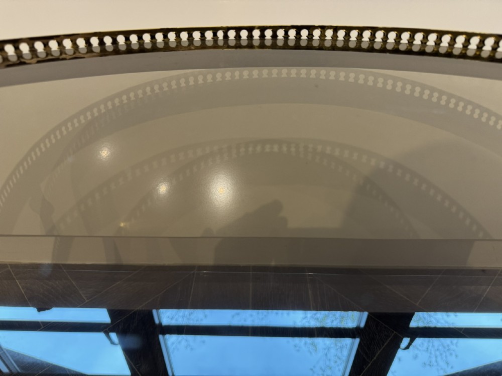A circular brass coffee table featuring a dark smoked glass top, a pierced gallery rim, turned legs, and a curved stretcher base. View IX
