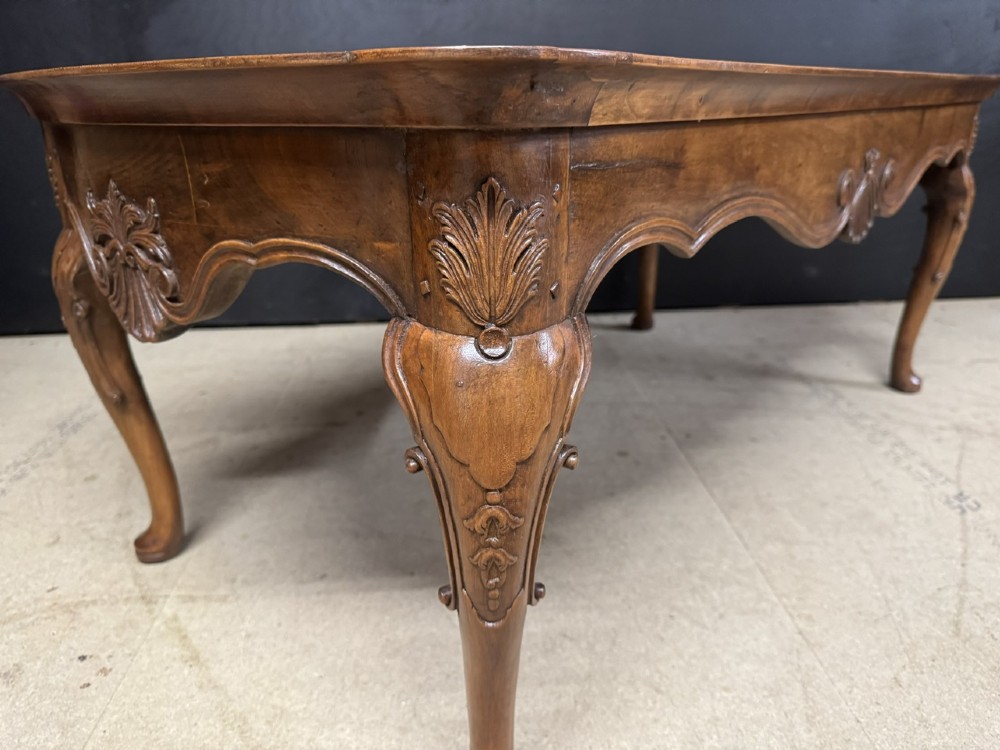 A burr walnut low coffee table featuring cabriole legs, a carved shell motif on the central apron, and a raised moulded edge around the top. View V