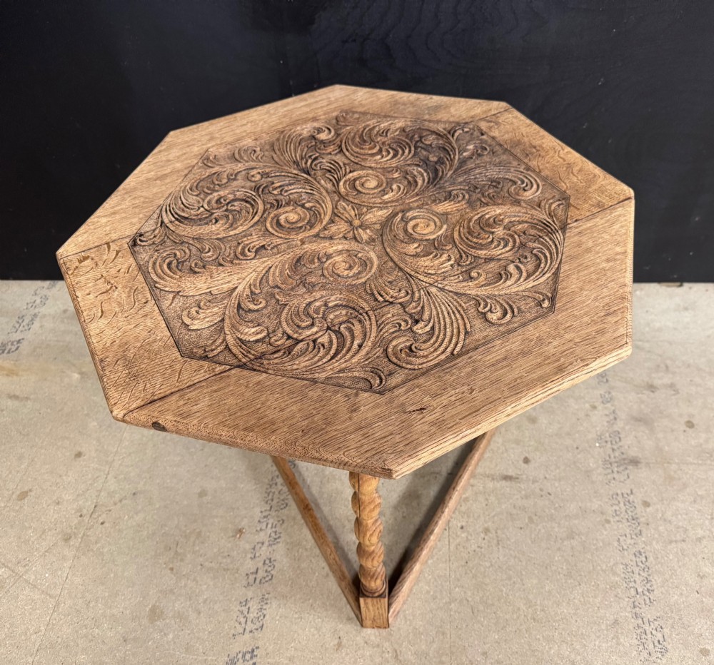 A hexagonal carved oak cricket table featuring elaborate foliate scrollwork on the tabletop and three turned legs joined by stretchers.