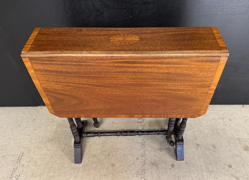 An Edwardian mahogany Sutherland table featuring drop leaves with satinwood crossbanding, central marquetry inlay, turned legs, and gateleg supports on castors. View II