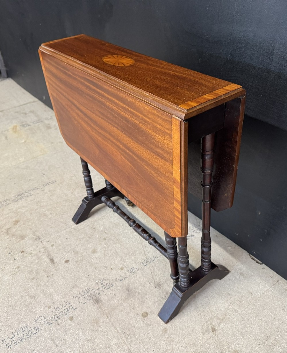 An Edwardian mahogany Sutherland table featuring drop leaves with satinwood crossbanding, central marquetry inlay, turned legs, and gateleg supports on castors. View III