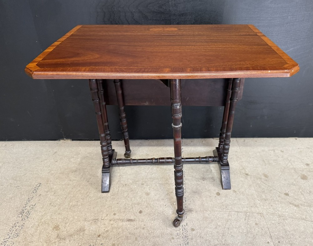 An Edwardian mahogany Sutherland table featuring drop leaves with satinwood crossbanding, central marquetry inlay, turned legs, and gateleg supports on castors. View V
