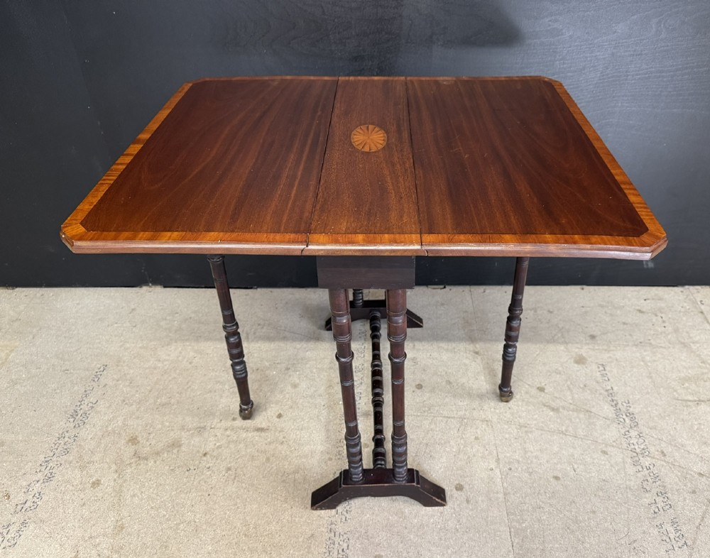 An Edwardian mahogany Sutherland table featuring drop leaves with satinwood crossbanding, central marquetry inlay, turned legs, and gateleg supports on castors. View VII