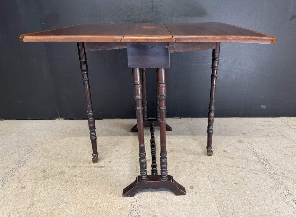 An Edwardian mahogany Sutherland table featuring drop leaves with satinwood crossbanding, central marquetry inlay, turned legs, and gateleg supports on castors. View VIII