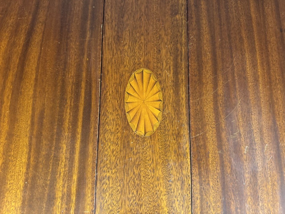 An Edwardian mahogany Sutherland table featuring drop leaves with satinwood crossbanding, central marquetry inlay, turned legs, and gateleg supports on castors. View IX