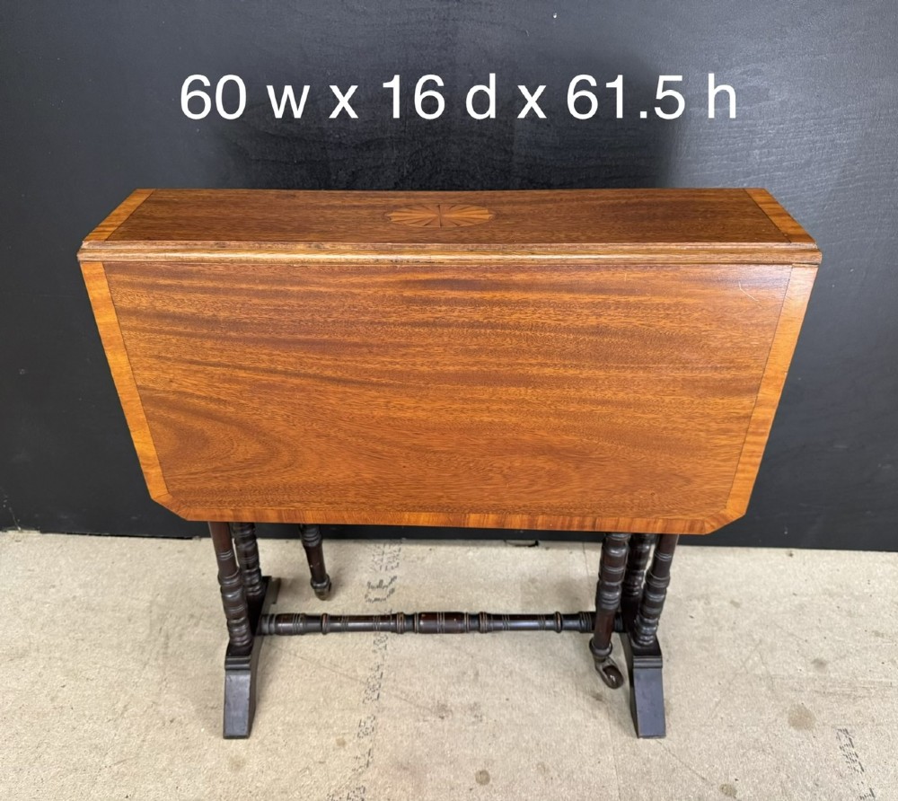 An Edwardian mahogany Sutherland table featuring drop leaves with satinwood crossbanding, central marquetry inlay, turned legs, and gateleg supports on castors. View XI