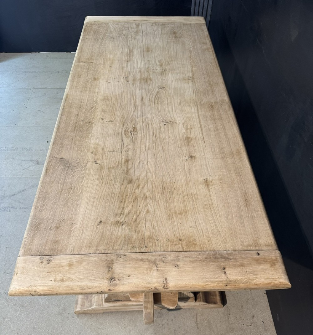 A large light oak farmhouse dining table featuring a solid plank top with breadboard ends supported by a shaped trestle base and a central stretcher rail. View III