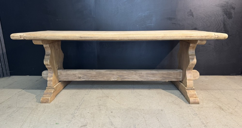A large light oak farmhouse dining table featuring a solid plank top with breadboard ends supported by a shaped trestle base and a central stretcher rail. View IV