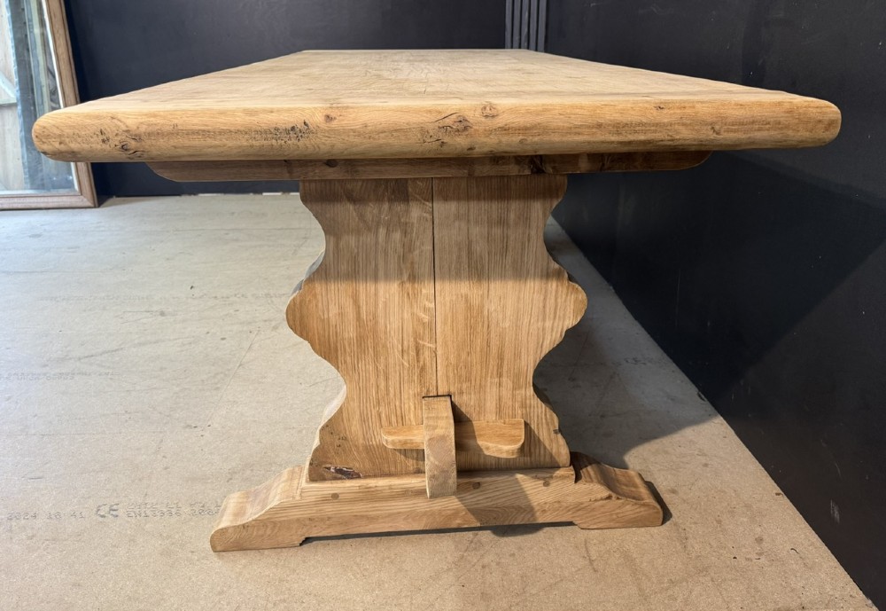 A large light oak farmhouse dining table featuring a solid plank top with breadboard ends supported by a shaped trestle base and a central stretcher rail. View VIII