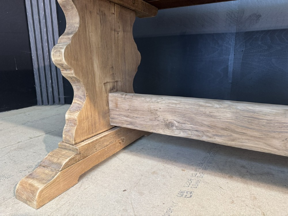 A large light oak farmhouse dining table featuring a solid plank top with breadboard ends supported by a shaped trestle base and a central stretcher rail. View XI