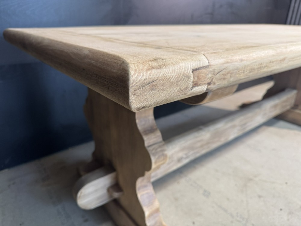 A large light oak farmhouse dining table featuring a solid plank top with breadboard ends supported by a shaped trestle base and a central stretcher rail. View XII