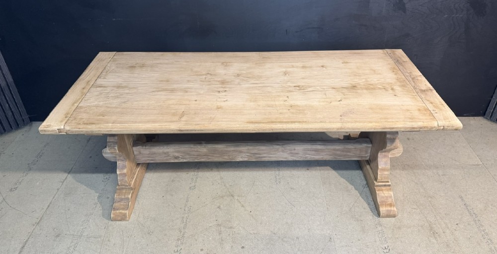 A large light oak farmhouse dining table featuring a solid plank top with breadboard ends supported by a shaped trestle base and a central stretcher rail. View XIII