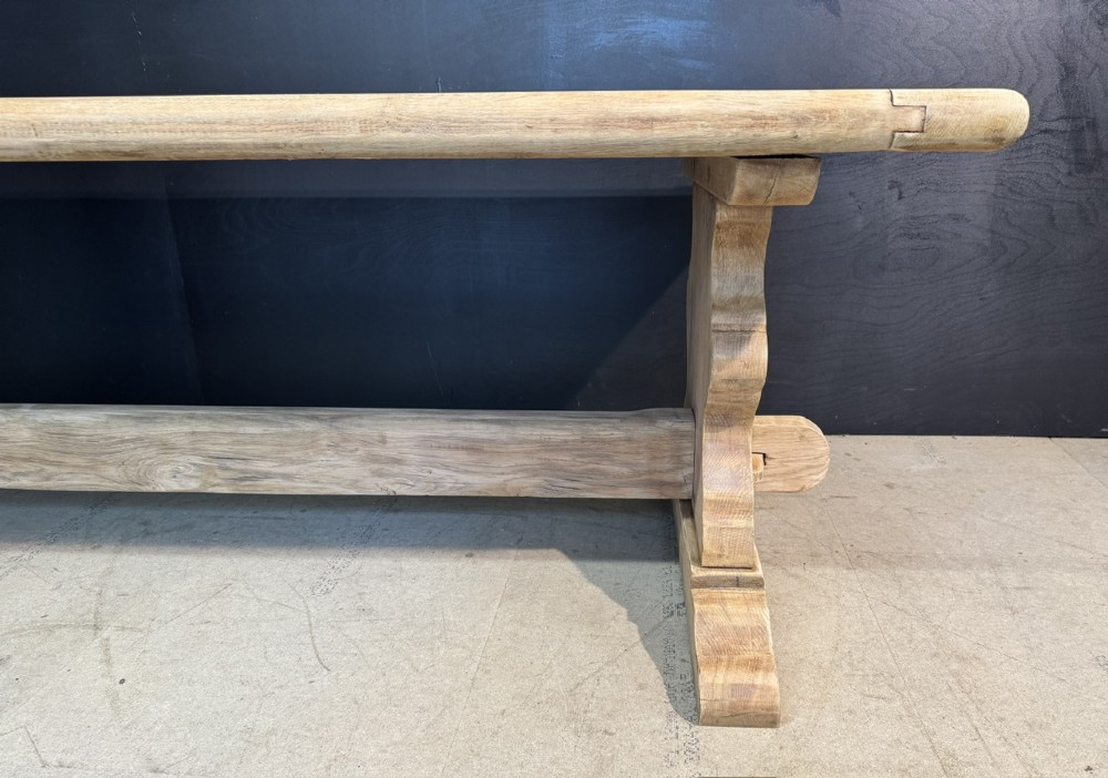 A large light oak farmhouse dining table featuring a solid plank top with breadboard ends supported by a shaped trestle base and a central stretcher rail. View XIV