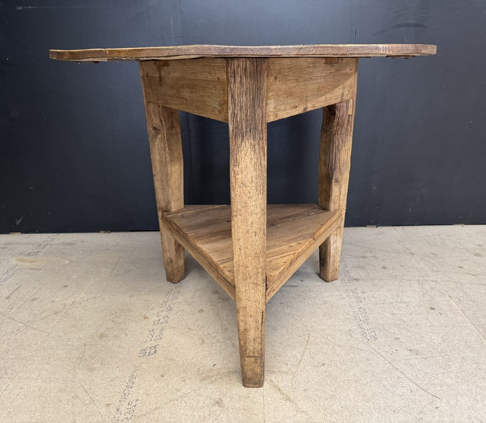 A rustic antique pine cricket table featuring a circular wooden top supported by three sturdy legs and a low triangular shelf. View II