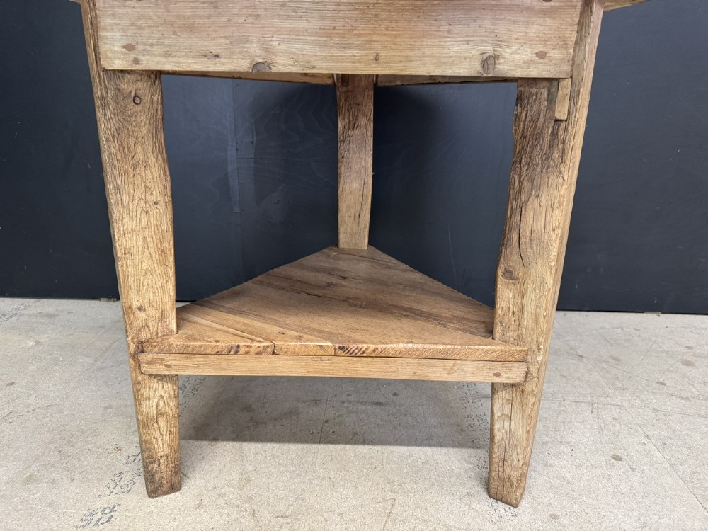 A rustic antique pine cricket table featuring a circular wooden top supported by three sturdy legs and a low triangular shelf. View VI
