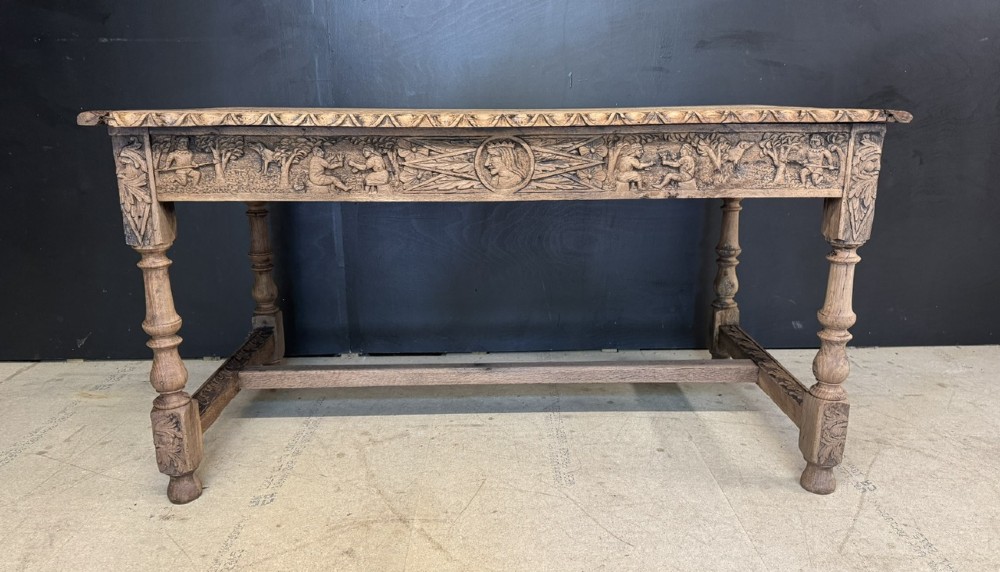 A light oak table featuring a detailed relief-carved frieze with human figures and a profile medallion, supported by turned legs and a central stretcher. View II
