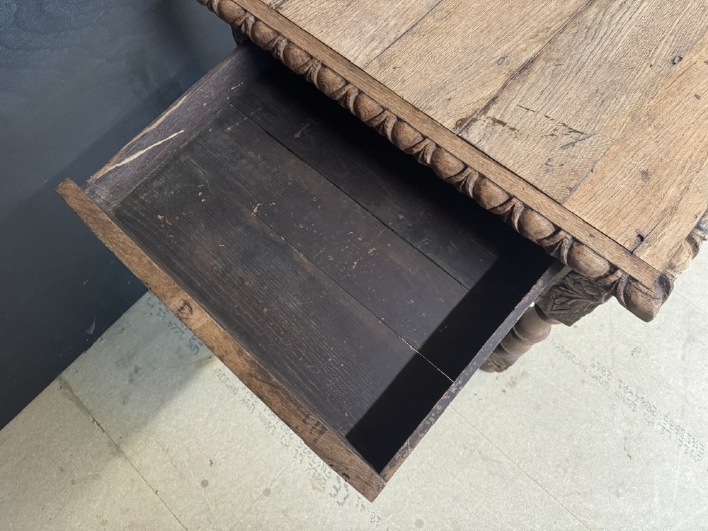 A light oak table featuring a detailed relief-carved frieze with human figures and a profile medallion, supported by turned legs and a central stretcher. View V