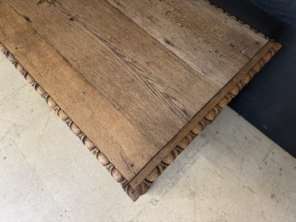 A light oak table featuring a detailed relief-carved frieze with human figures and a profile medallion, supported by turned legs and a central stretcher. View VI
