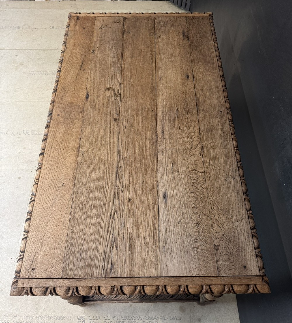 A light oak table featuring a detailed relief-carved frieze with human figures and a profile medallion, supported by turned legs and a central stretcher. View VII