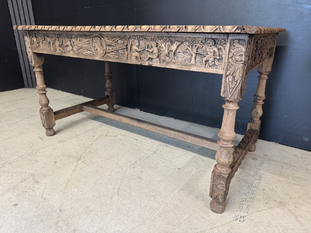 A light oak table featuring a detailed relief-carved frieze with human figures and a profile medallion, supported by turned legs and a central stretcher. View XIII