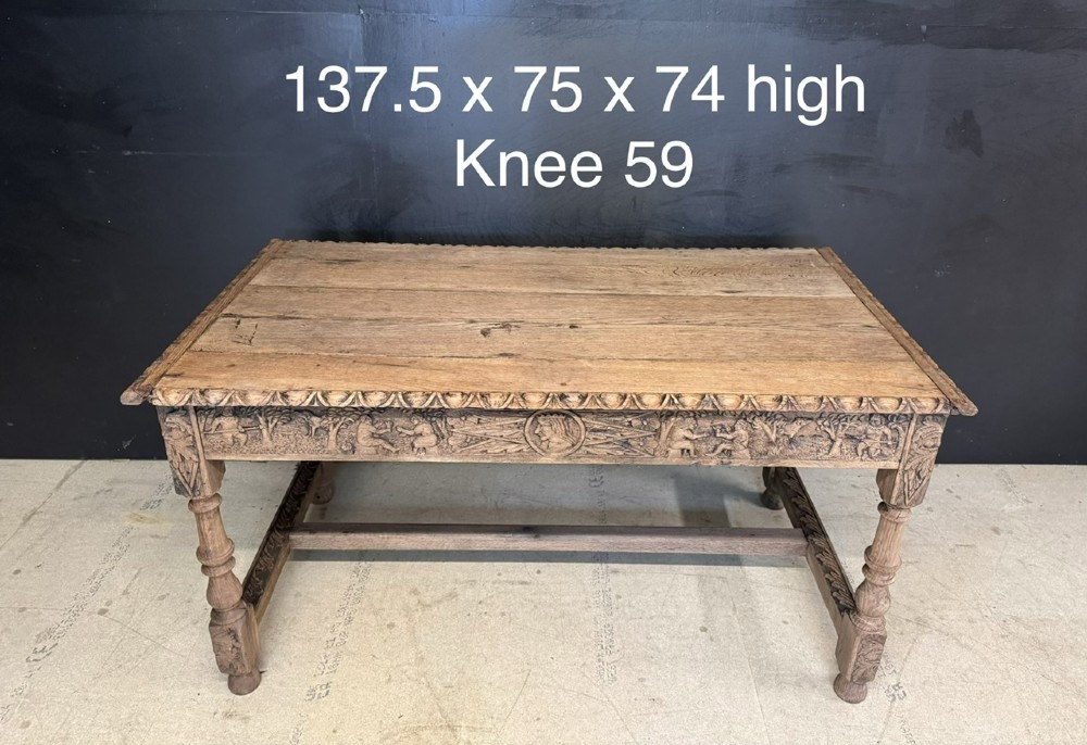 A light oak table featuring a detailed relief-carved frieze with human figures and a profile medallion, supported by turned legs and a central stretcher. View XIV