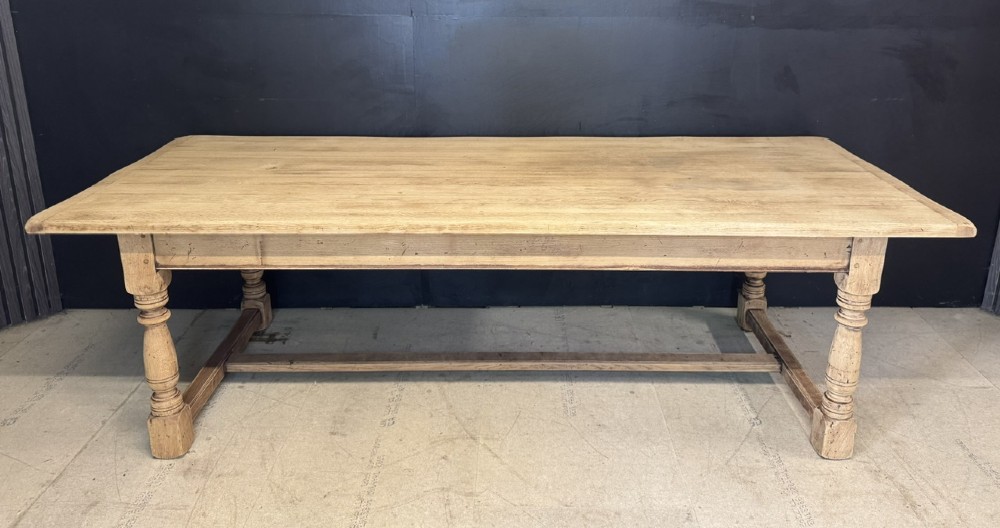 Large rectangular light oak farmhouse dining table featuring turned legs and an H-stretcher base.