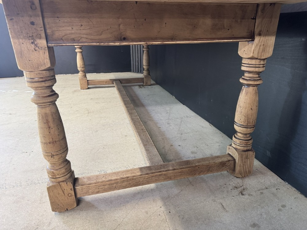 Large rectangular light oak farmhouse dining table featuring turned legs and an H-stretcher base. View IX