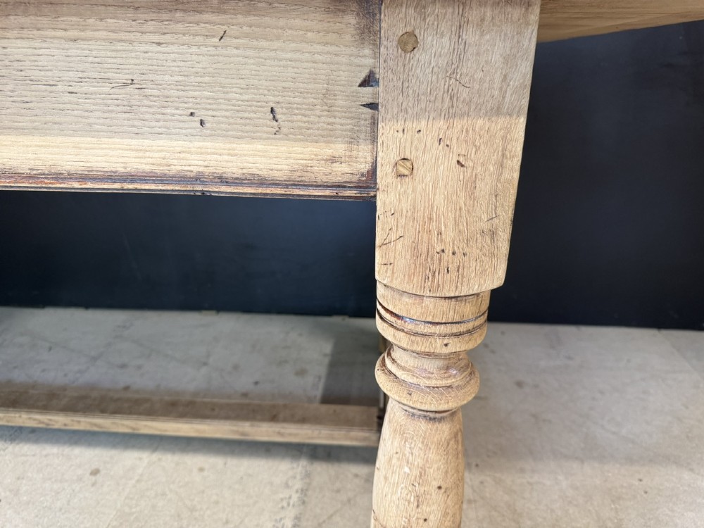 Large rectangular light oak farmhouse dining table featuring turned legs and an H-stretcher base. View X