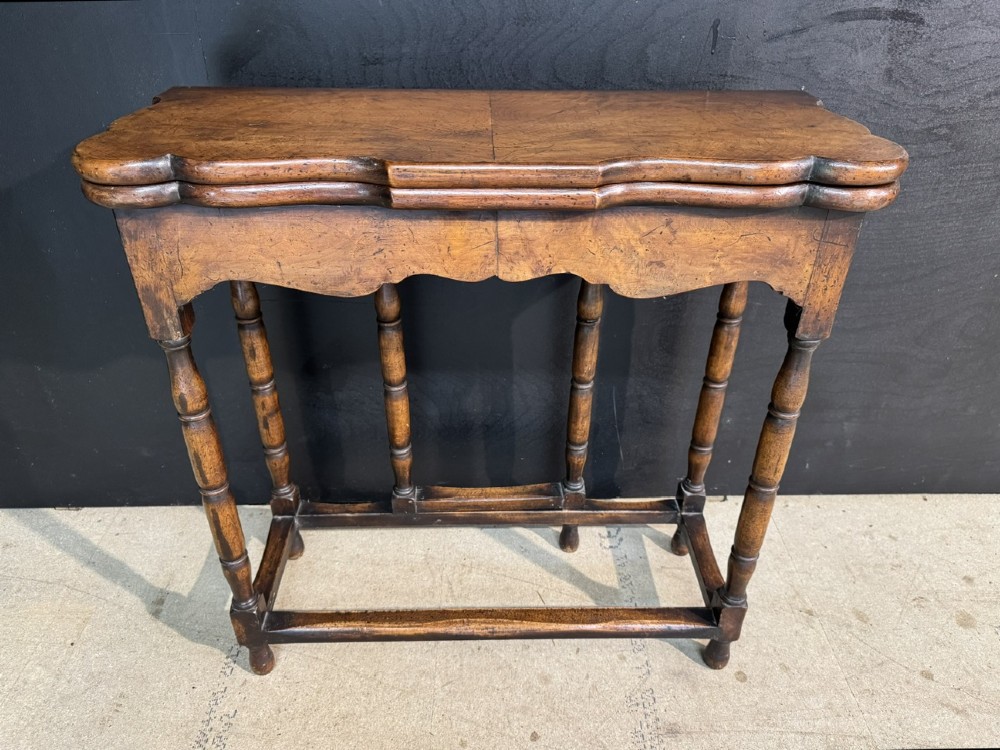 An antique walnut fold-over tea table with a shaped double top, contoured frieze, turned legs, and a lower box stretcher.