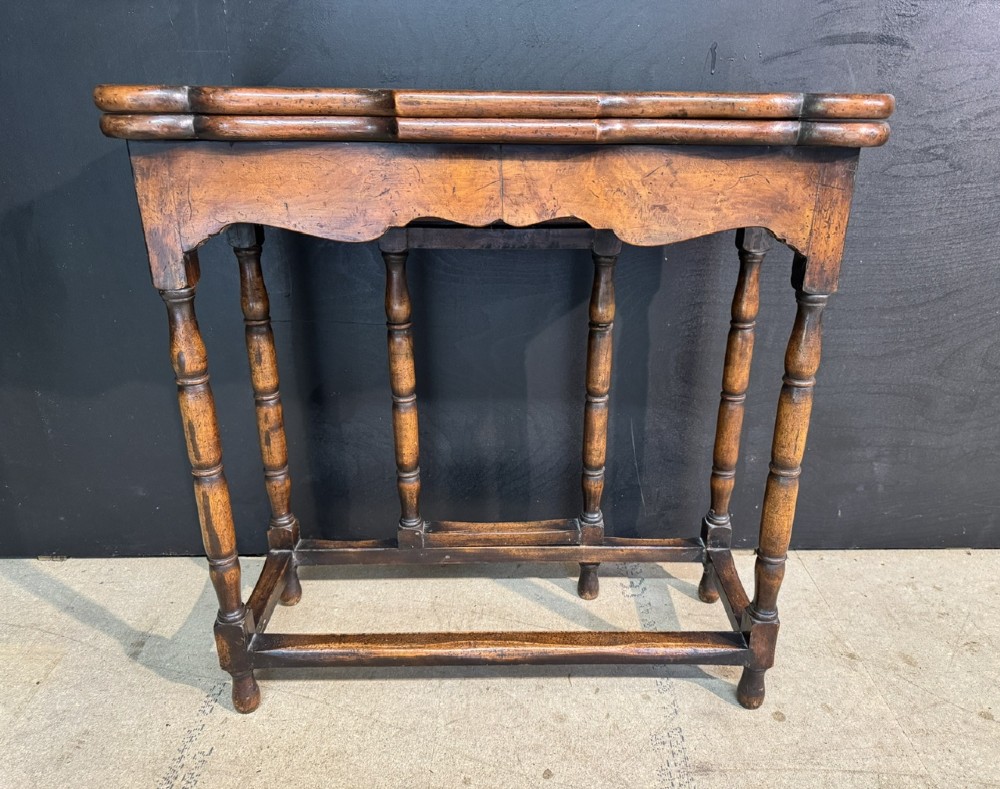 An antique walnut fold-over tea table with a shaped double top, contoured frieze, turned legs, and a lower box stretcher. View II