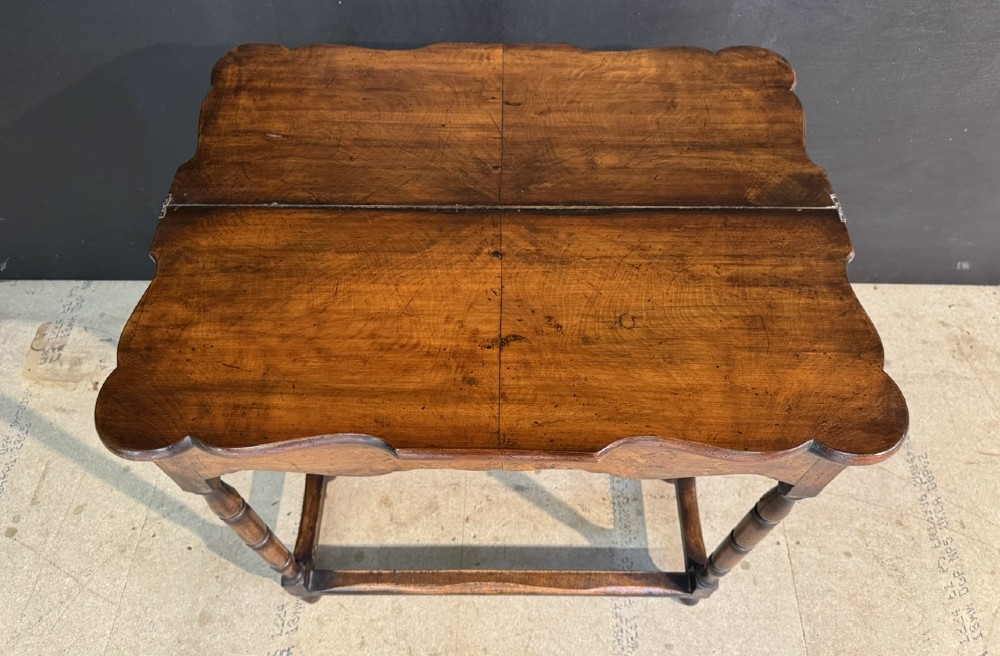 An antique walnut fold-over tea table with a shaped double top, contoured frieze, turned legs, and a lower box stretcher. View VI
