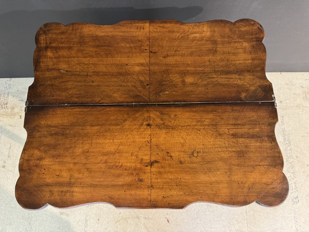 An antique walnut fold-over tea table with a shaped double top, contoured frieze, turned legs, and a lower box stretcher. View VII