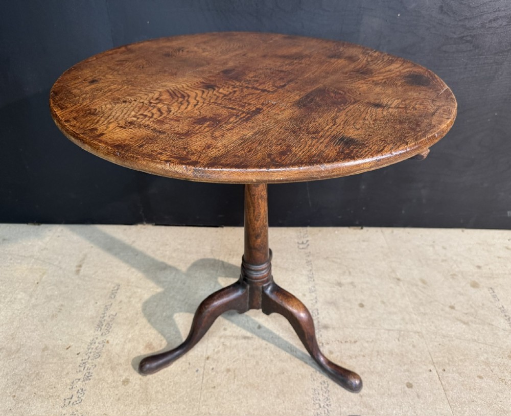 A Georgian solid oak tilt-top table with a circular surface supported by a turned pedestal column and three cabriole tripod legs.
