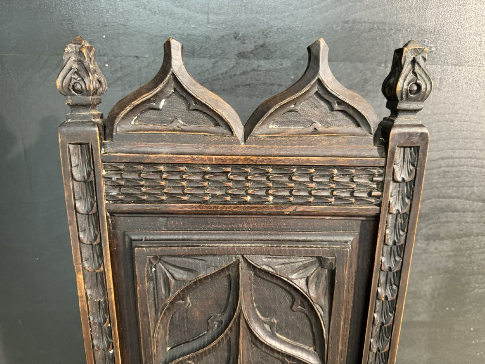 An antique dark oak open armchair featuring a tall carved back panel decorated with Gothic tracery motifs, curved armrests, and turned front legs. View IV