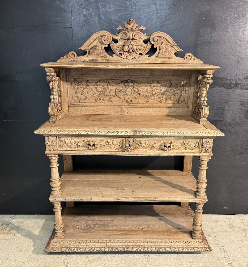 A 19th-century French carved oak buffet featuring an ornate crest, open shelf, turned columns, and carved drawers.