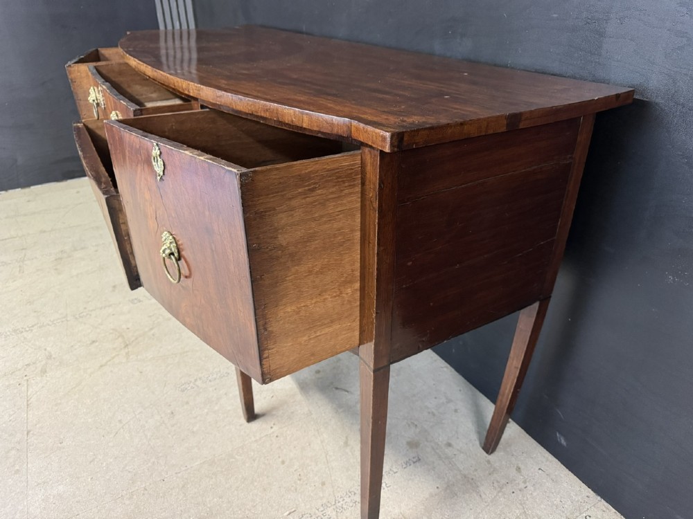An antique Georgian mahogany bow-front sideboard featuring a central drawer, flanking cupboard doors, brass lion mask ring handles, and square tapered legs. View V
