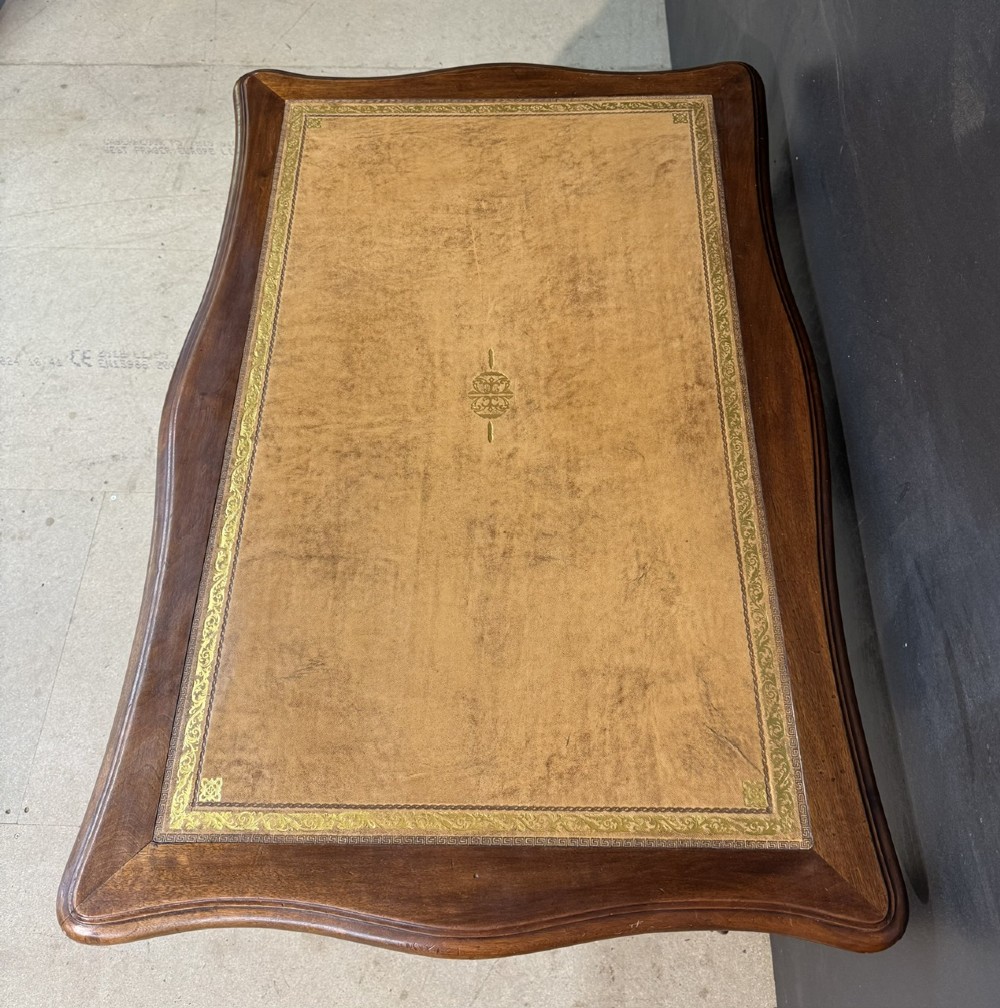 A French Rococo style writing desk crafted from carved light brown wood with a tan leather top, cabriole legs, and a carved drawer front. View IV