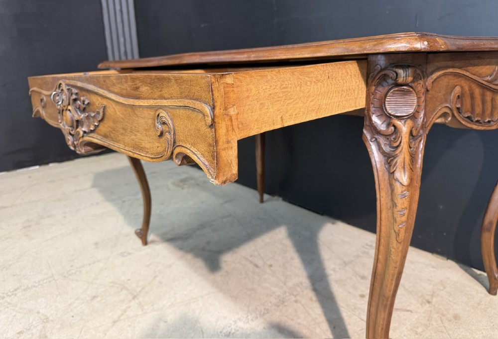 A French Rococo style writing desk crafted from carved light brown wood with a tan leather top, cabriole legs, and a carved drawer front. View VII