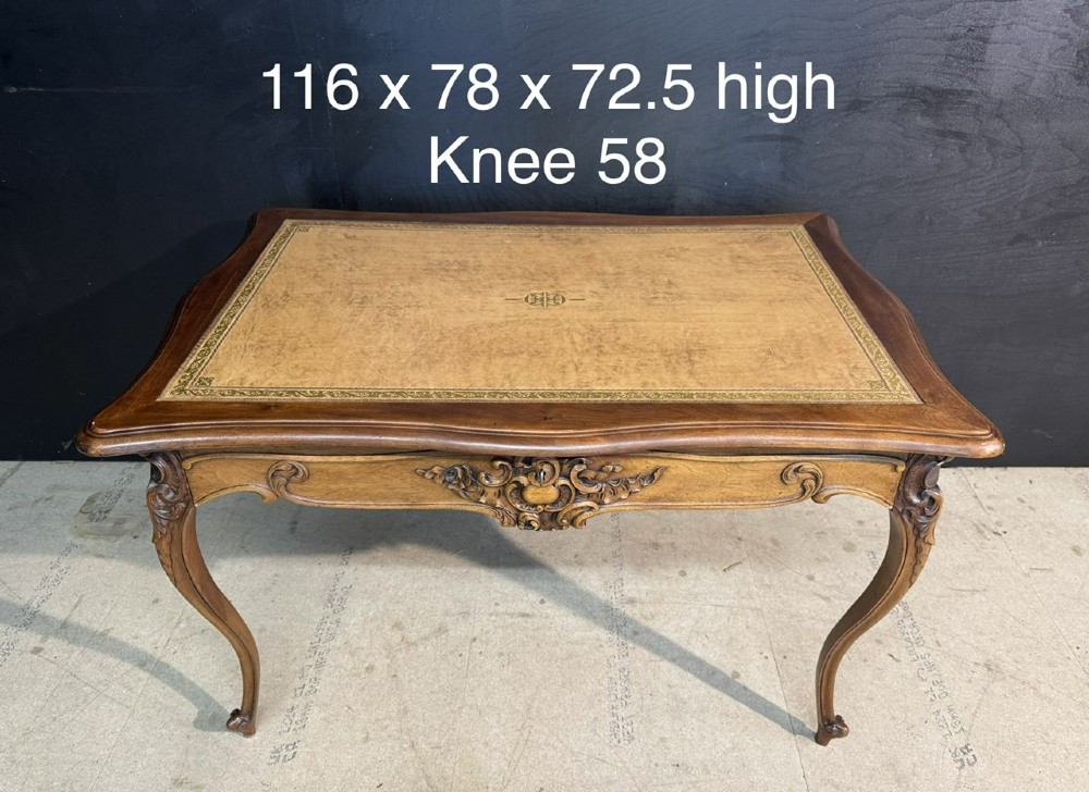 A French Rococo style writing desk crafted from carved light brown wood with a tan leather top, cabriole legs, and a carved drawer front. View X