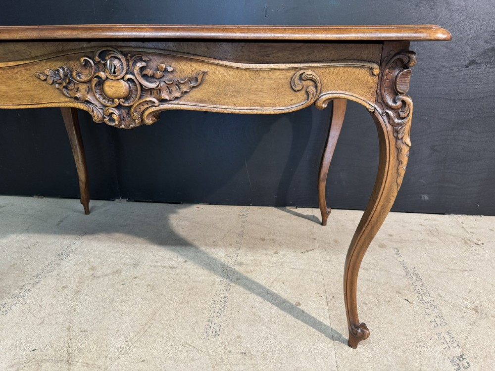 A French Rococo style writing desk crafted from carved light brown wood with a tan leather top, cabriole legs, and a carved drawer front. View XIII