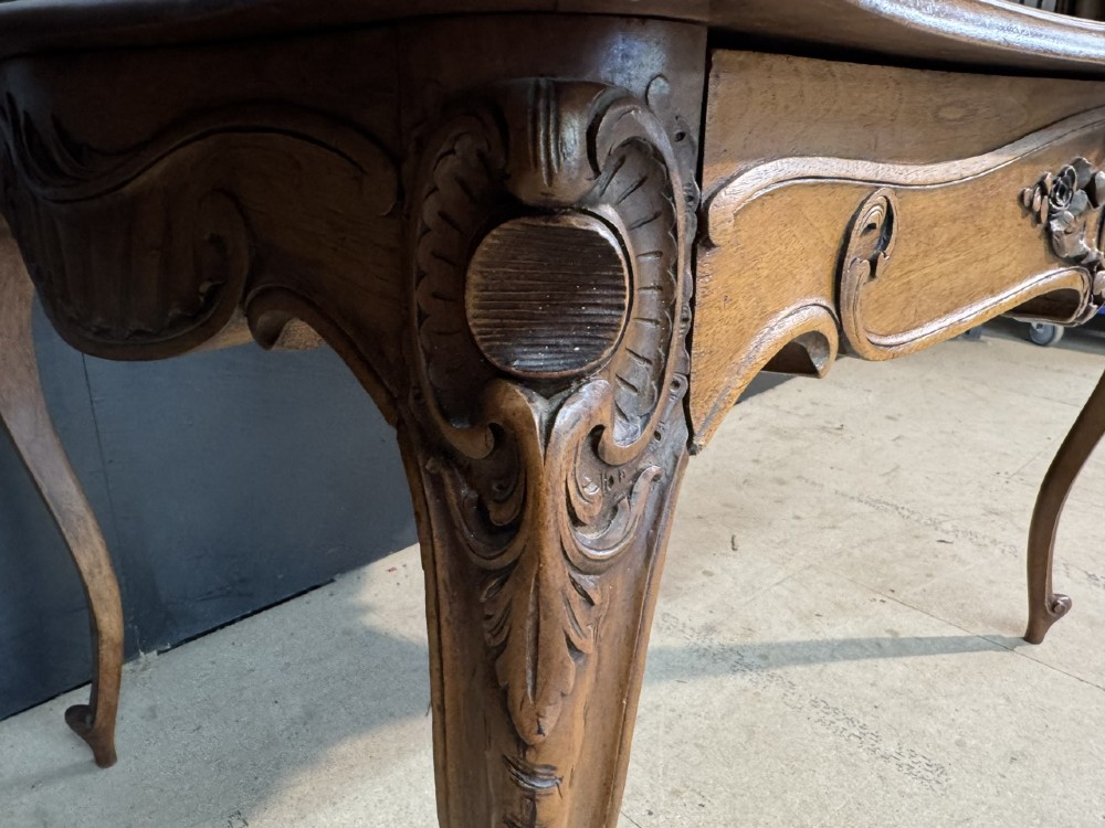 A French Rococo style writing desk crafted from carved light brown wood with a tan leather top, cabriole legs, and a carved drawer front. View XIV