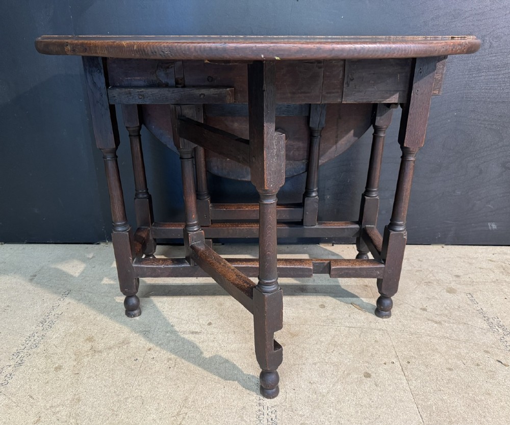 An eighteenth-century dark oak gateleg table featuring an oval drop-leaf top supported by turned legs and stretchers. View XI