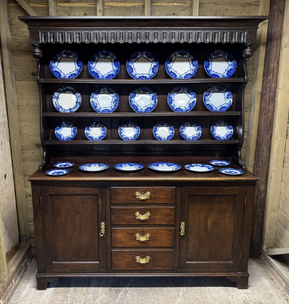 A dark oak Welsh dresser featuring a three-tier open plate rack canopy atop a base with four central drawers flanked by two panelled cupboard doors with brass handles.
