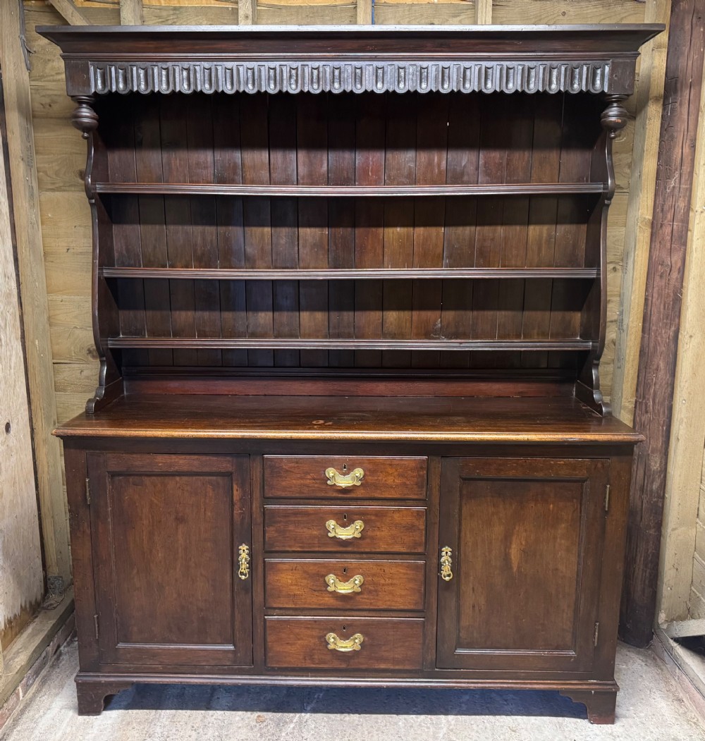 A dark oak Welsh dresser featuring a three-tier open plate rack canopy atop a base with four central drawers flanked by two panelled cupboard doors with brass handles. View II