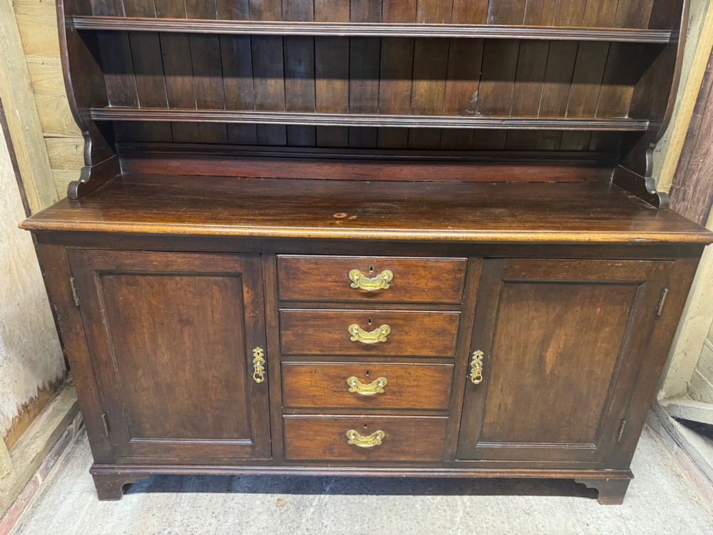 A dark oak Welsh dresser featuring a three-tier open plate rack canopy atop a base with four central drawers flanked by two panelled cupboard doors with brass handles. View III
