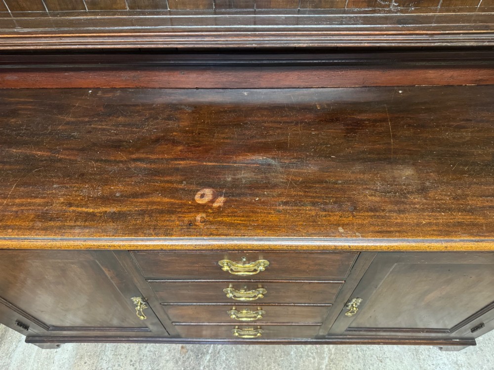 A dark oak Welsh dresser featuring a three-tier open plate rack canopy atop a base with four central drawers flanked by two panelled cupboard doors with brass handles. View VII