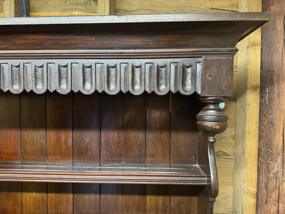 A dark oak Welsh dresser featuring a three-tier open plate rack canopy atop a base with four central drawers flanked by two panelled cupboard doors with brass handles. View VIII