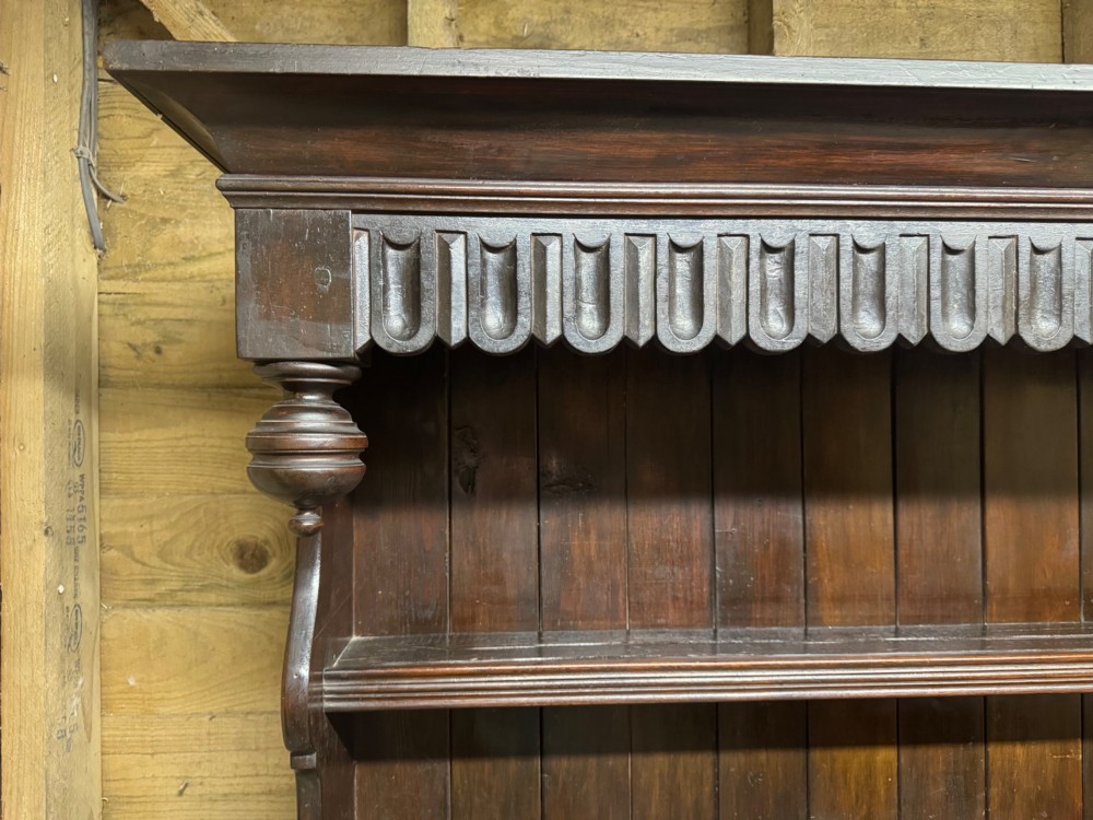 A dark oak Welsh dresser featuring a three-tier open plate rack canopy atop a base with four central drawers flanked by two panelled cupboard doors with brass handles. View IX