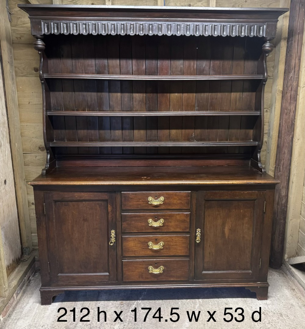 A dark oak Welsh dresser featuring a three-tier open plate rack canopy atop a base with four central drawers flanked by two panelled cupboard doors with brass handles. View XI